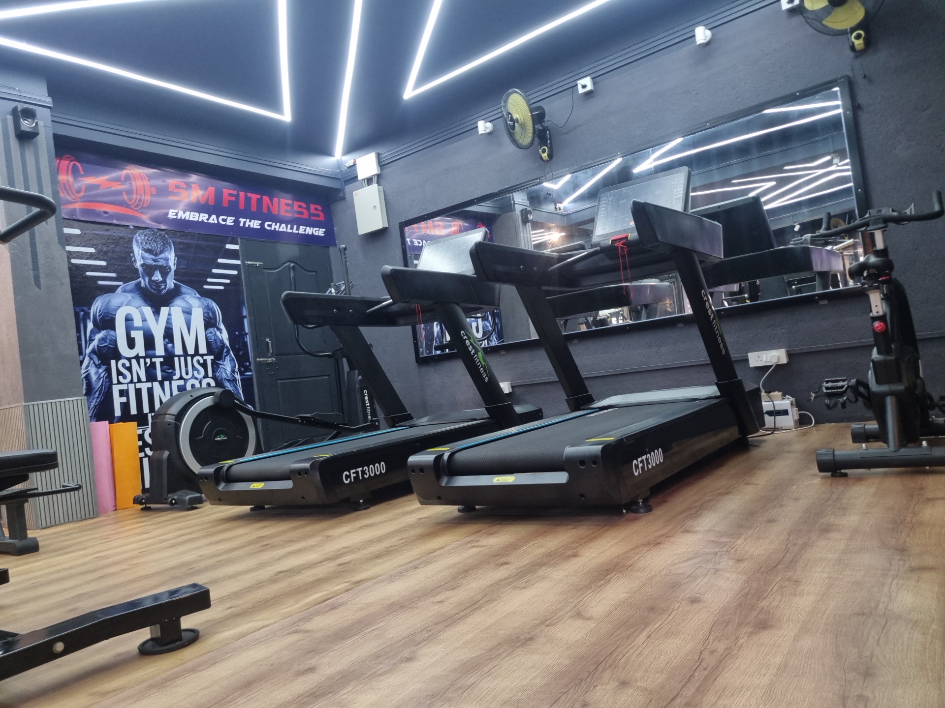 Treadmills on a wood floor at SM Fitness, under white LED lines set into a dark ceiling